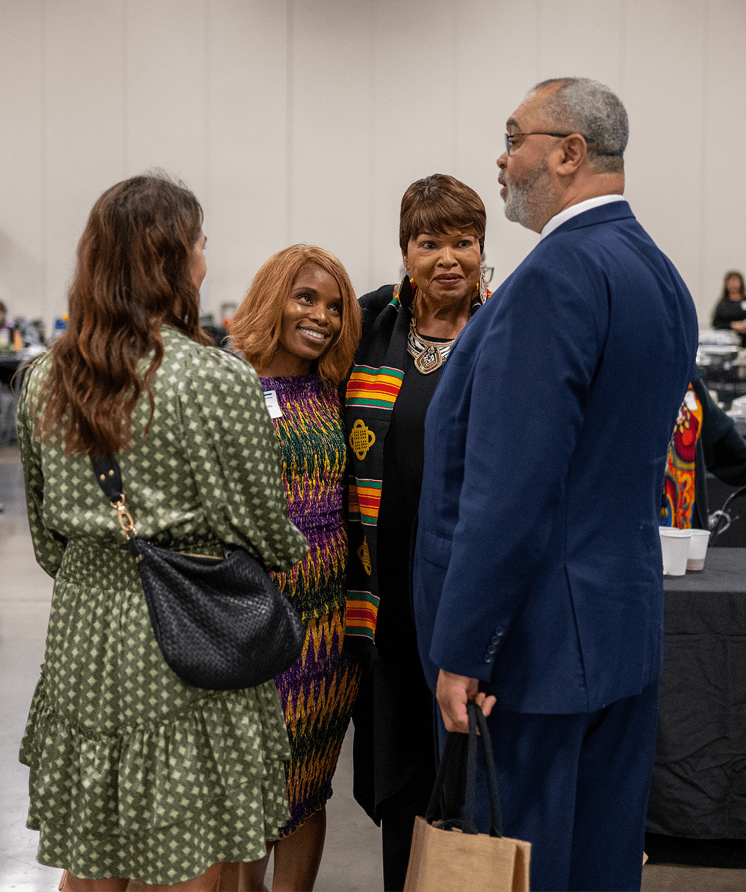 Four individuals engage in conversation at an event, with one woman wearing a colorful garment. Their expressions suggest a warm exchange.