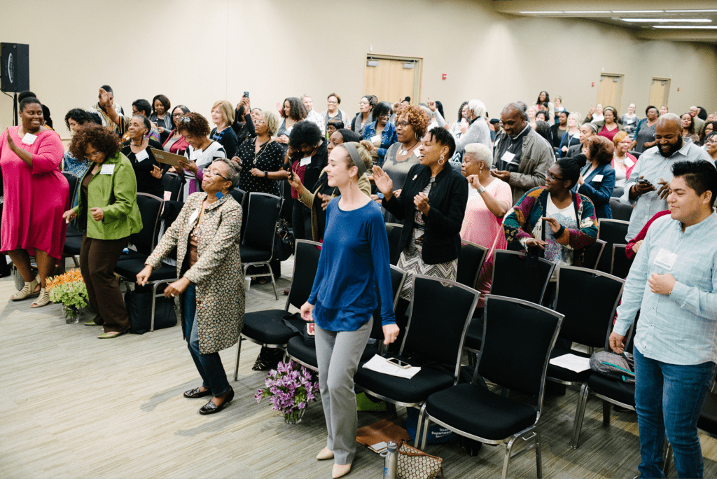 Participants joyfully engaging in an interactive session at a conference, showcasing enthusiasm and community spirit in a packed room.