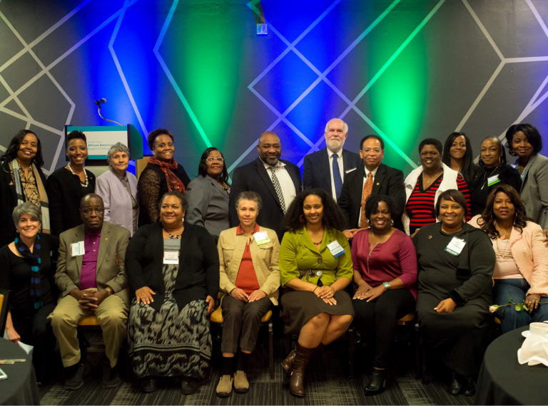 Group portrait of diverse attendees at an African American leadership conference, smiling and engaging, with a colorful backdrop.